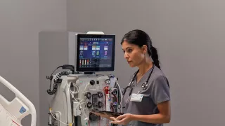 Clinician stands at the bedside in front of the PrisMax System