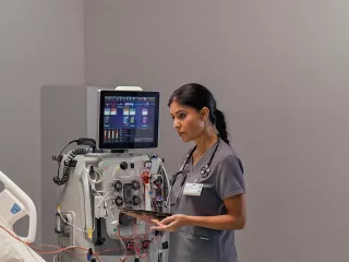 Healthcare professional at the patient bedside in front of the PrisMax System